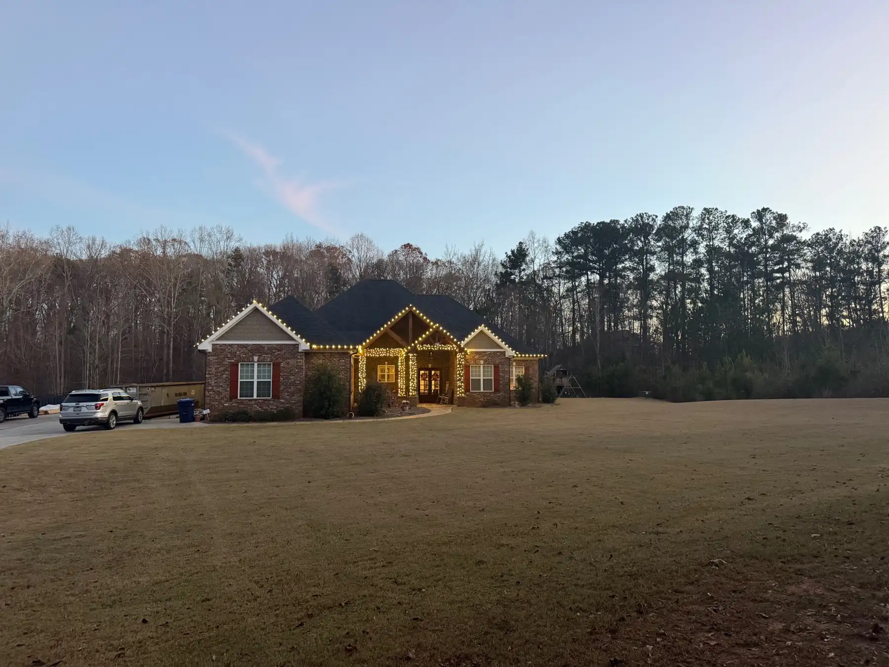 Brick ranch home at dusk with warm white bulbs along the front gables and the porch posts and beams wrapped in lights