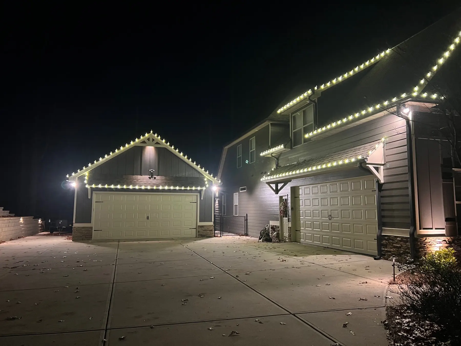 Two garages at night, each gable and eave outlined in evenly spaced warm white C9 bulbs across a shared concrete drive